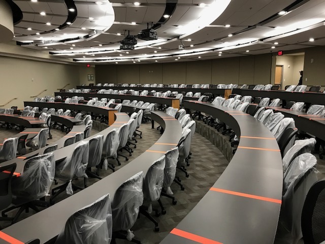 Tape and covered chairs indicate which seats and portions of a table are unavailable to students in a socially distanced lecture hall.