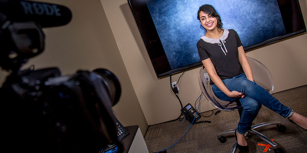 Sasha Peshwani sits in a chair in front of a blue screen as her photo is taken