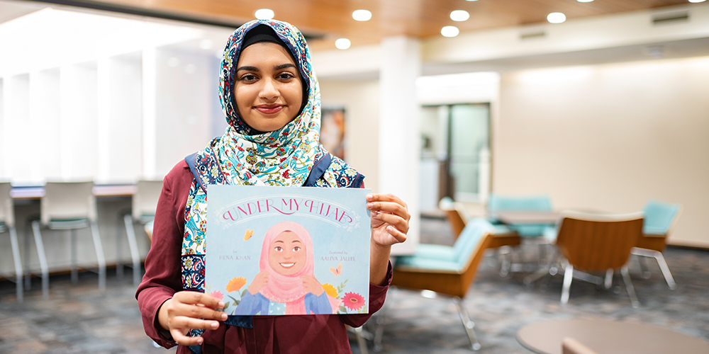 Woman wearing a hijab holding a book she illustrated