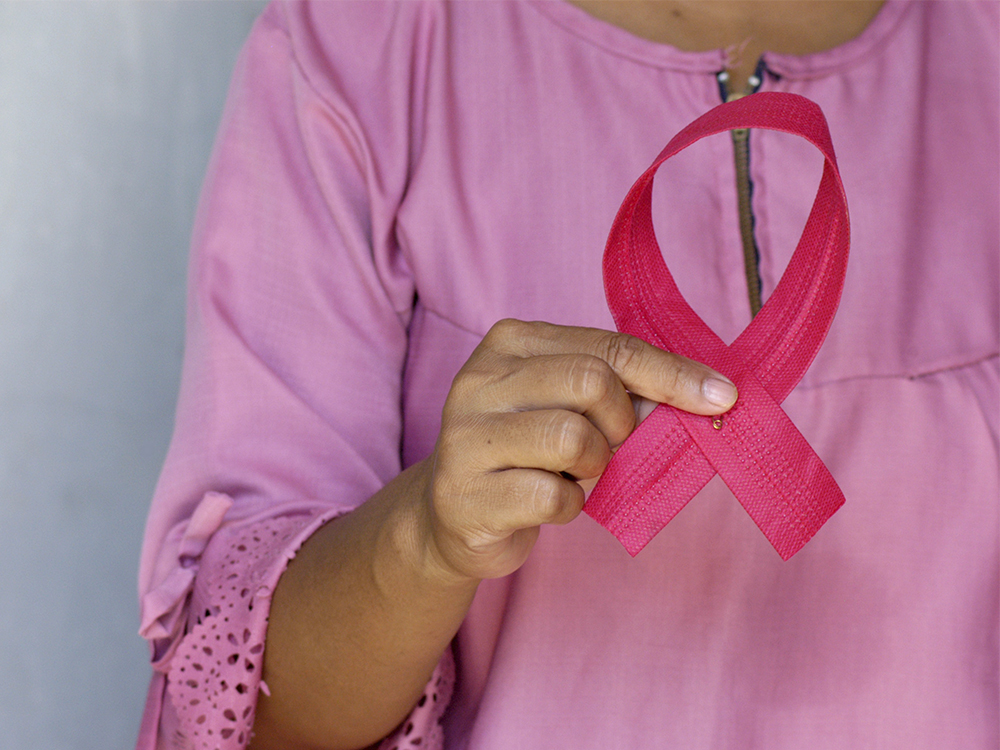A woman holds up a large pink ribbon in honor of Breast Cancer Awareness Month