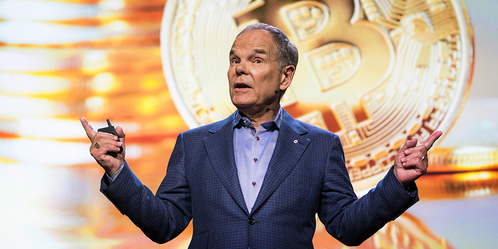 Photo of Don Tapscott standing on stage in front of the Bitcoin logo