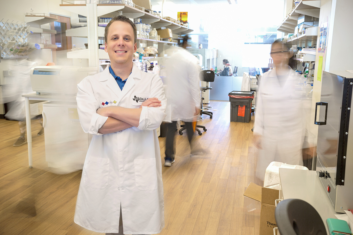 Dr. Zachary Campbell smiles in a lab as researchers walk around him