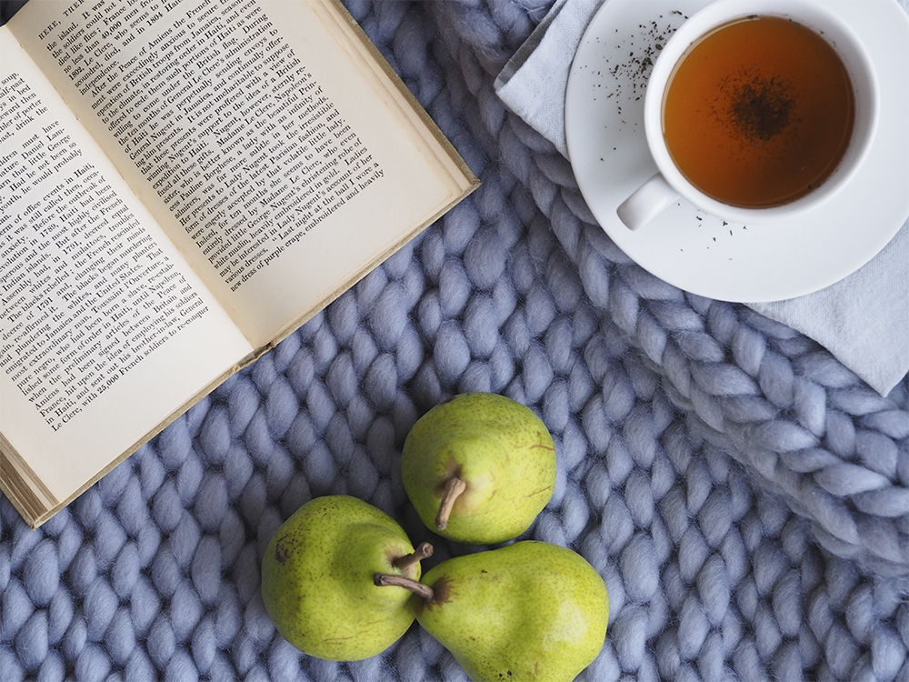 A handful of pears, a cup of tea and an open book sit on a desk