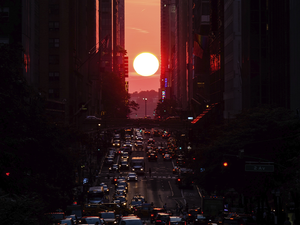 The sun sets between two rows of skyscrapers with cars on a street in between