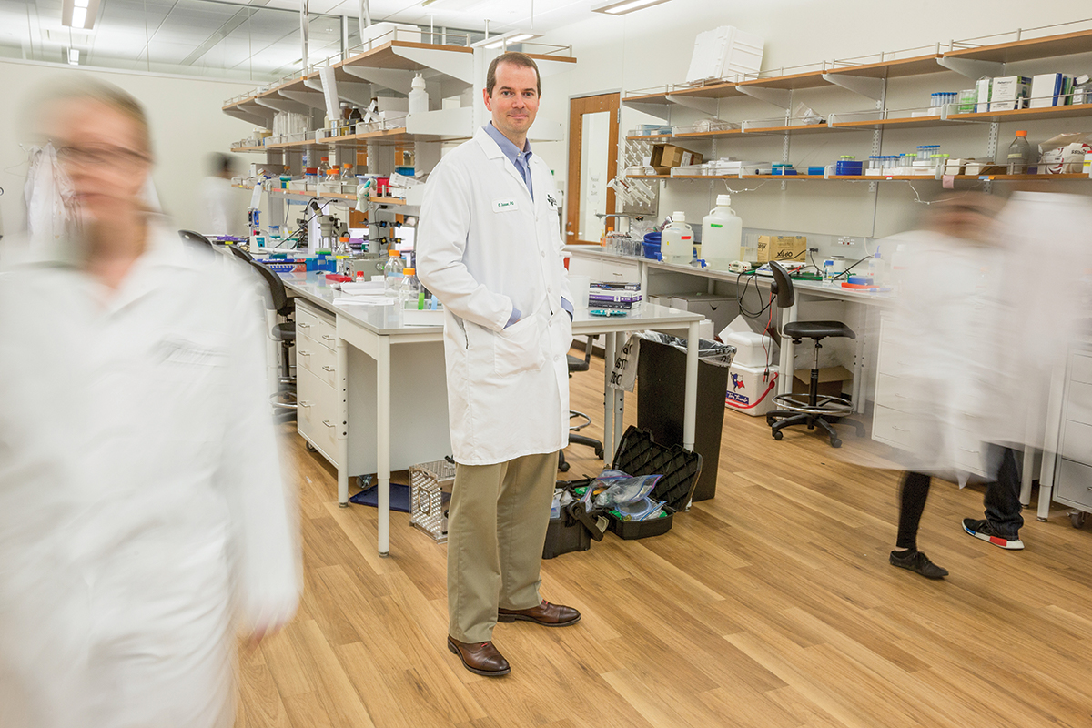 Dr. Greg Dussor stands in a lab as researchers walk past him