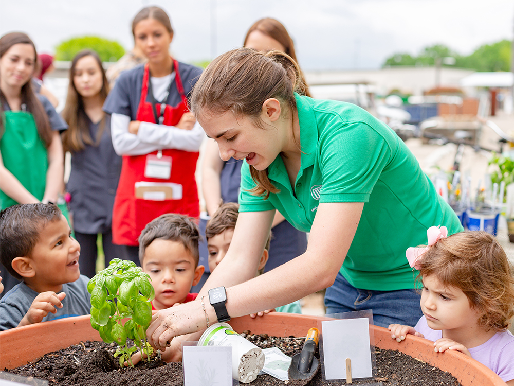 College student planting flowers with young children