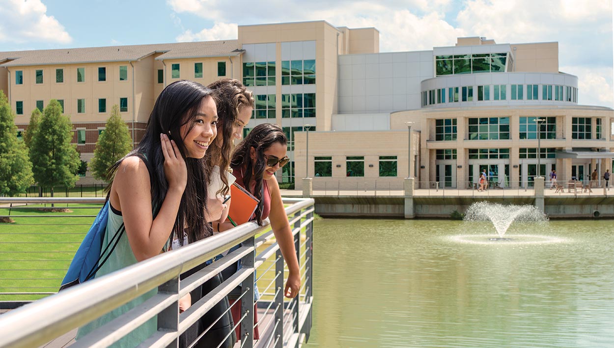 A group of students lean against a railing near the pond at Dining Hall West