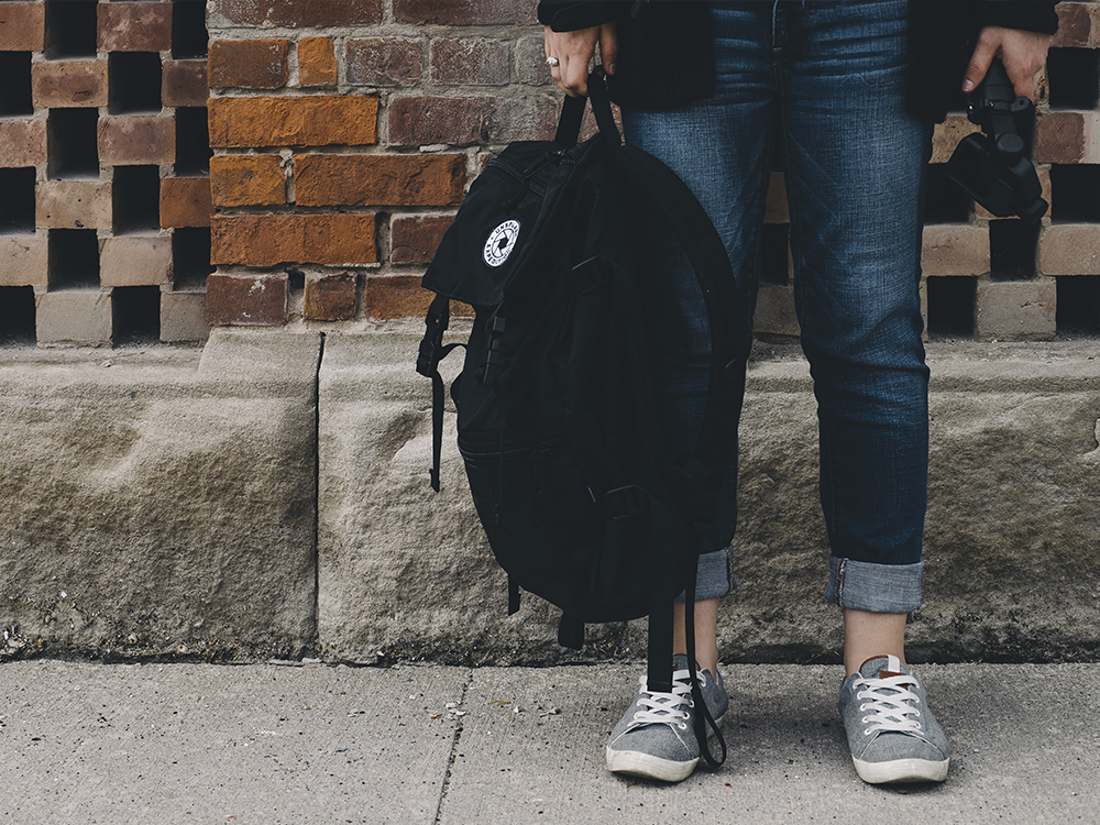 Person holding a backpack in front of a brick wall