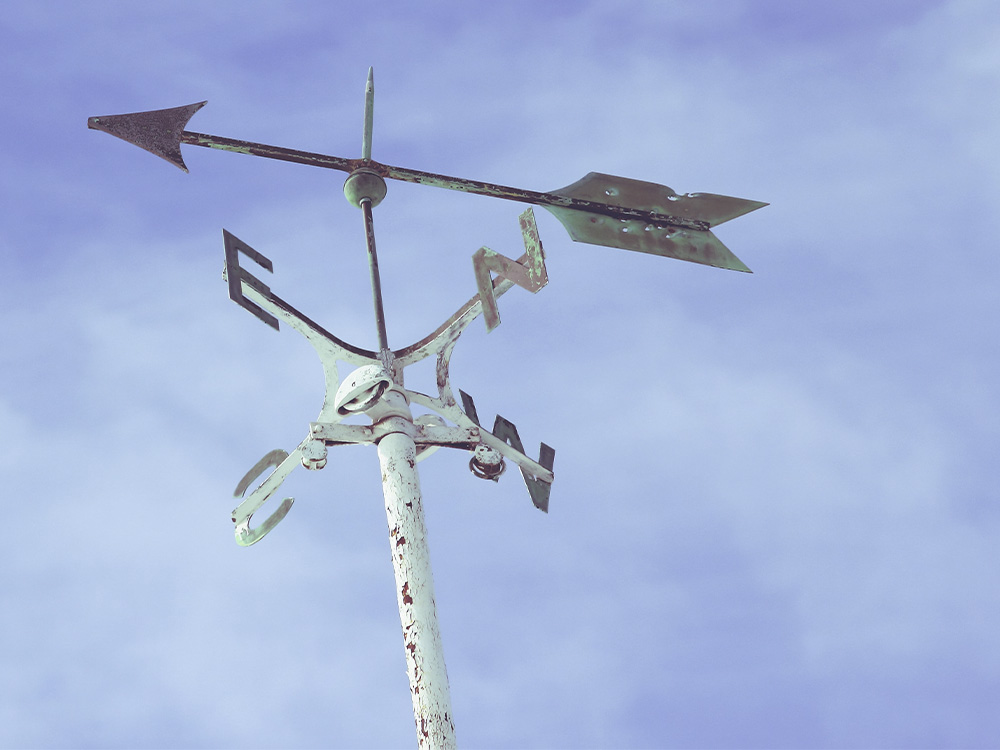 A weather vane with wisps of clouds behind it in a blue sky.