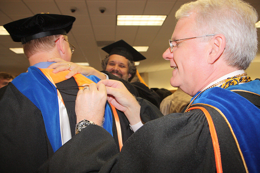 Dr. Bruce Novak, dean of the School of Natural Sciences and Mathematics, adjusts the academic hood for a new PhD graduate during a reception for 65 spring doctoral graduates at UT Dallas.