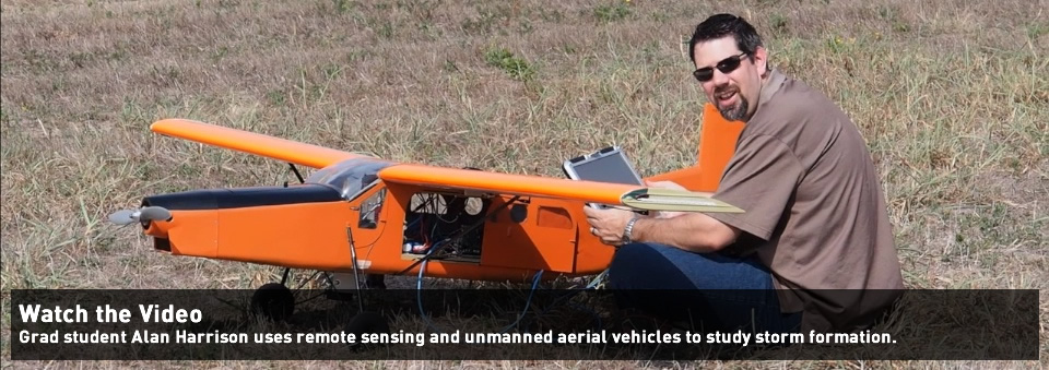 A student prepares a remote-controlled plane for flight in a field.